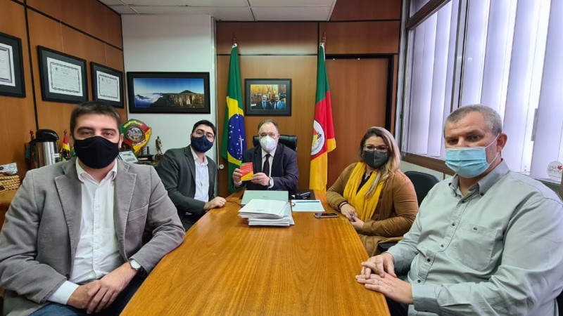 Cinco pessoas, quatro homens e uma mulher, sentados em reunião. O homem ao centro segura o código de defesa do consumidor.