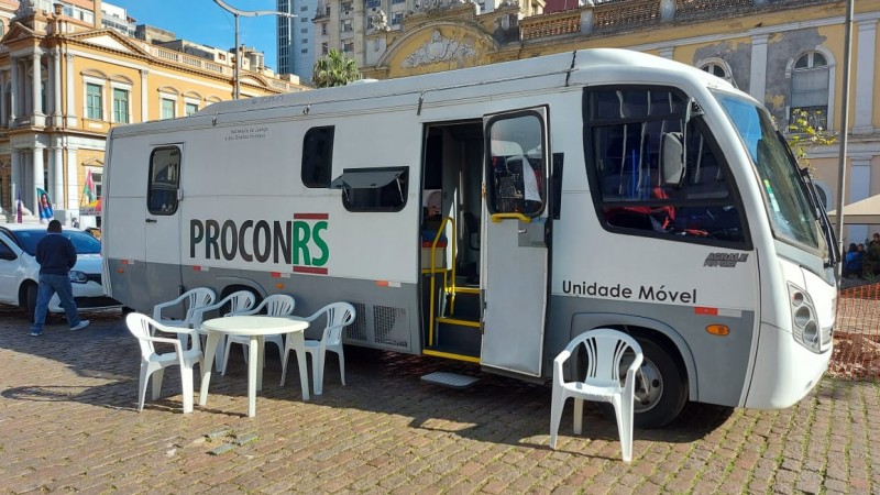 Ônibus branco estacionado com cadeiras na frente. Na lateral do ônibus se lê Procon RS.