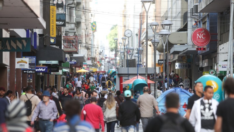 Na foto, há várias pessoas caminhando pela Rua dos Andradas, Centro Histórico de Porto Alegre, e diversos estabelecimentos comerciais.