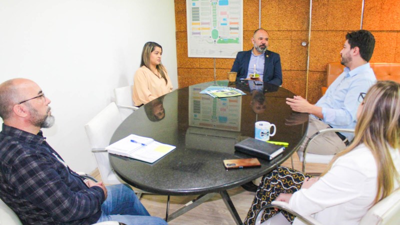 As autoridades estão reunidas ao redor de uma mesa circular da cor preta. Na foto o Diretor Rainer fala observando o presidente da Ceasa/RS.